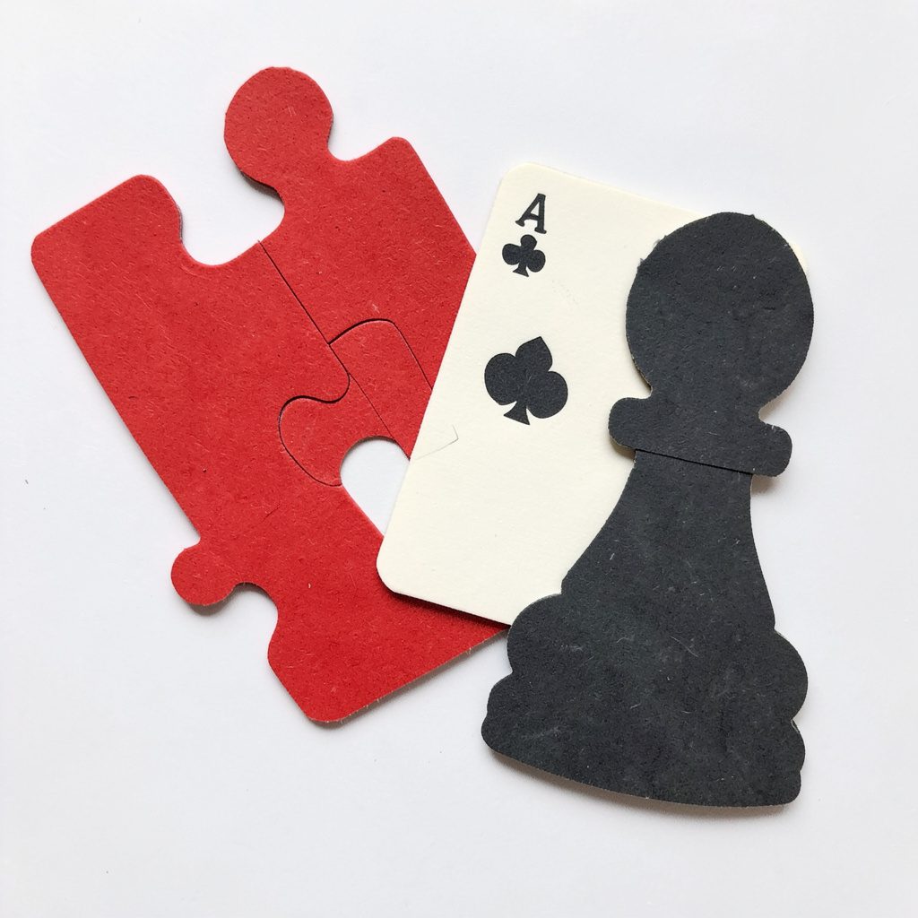 A layered paper cut-out collage of game pieces in crimson red, cream white and charcoal black, showing a stylized puzzle