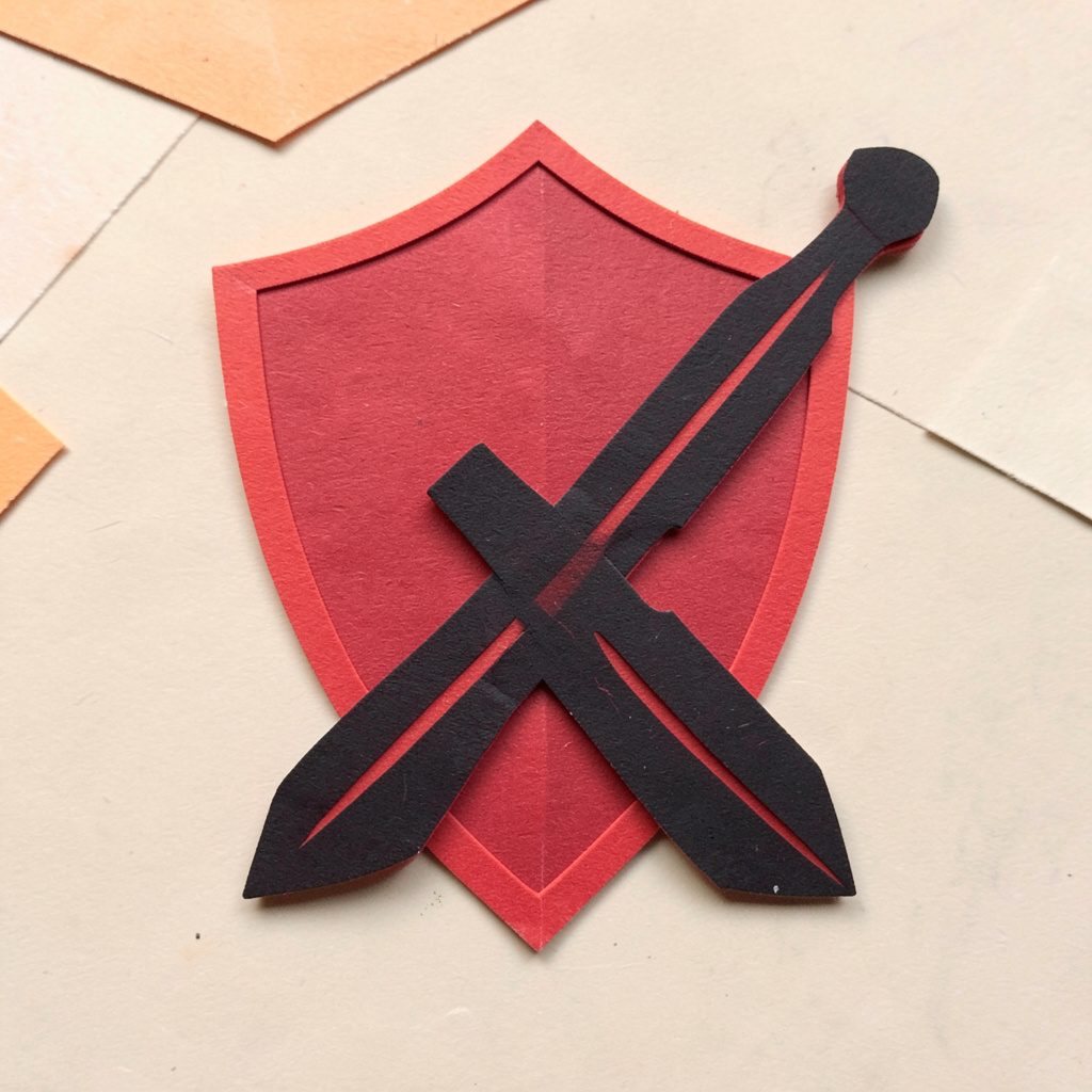 A small layered paper cut-out collage of a shield and sword crossed in crimson red and black, heroic mood