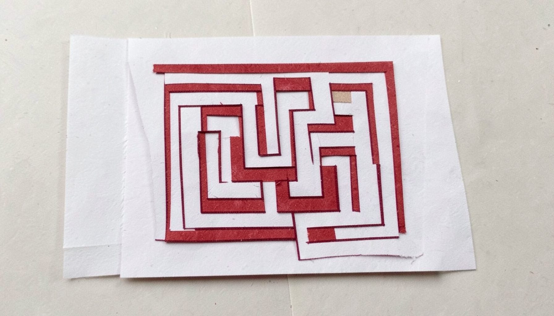 A small layered paper cut-out collage of a maze pattern in dark red lines on white paper, puzzling mood