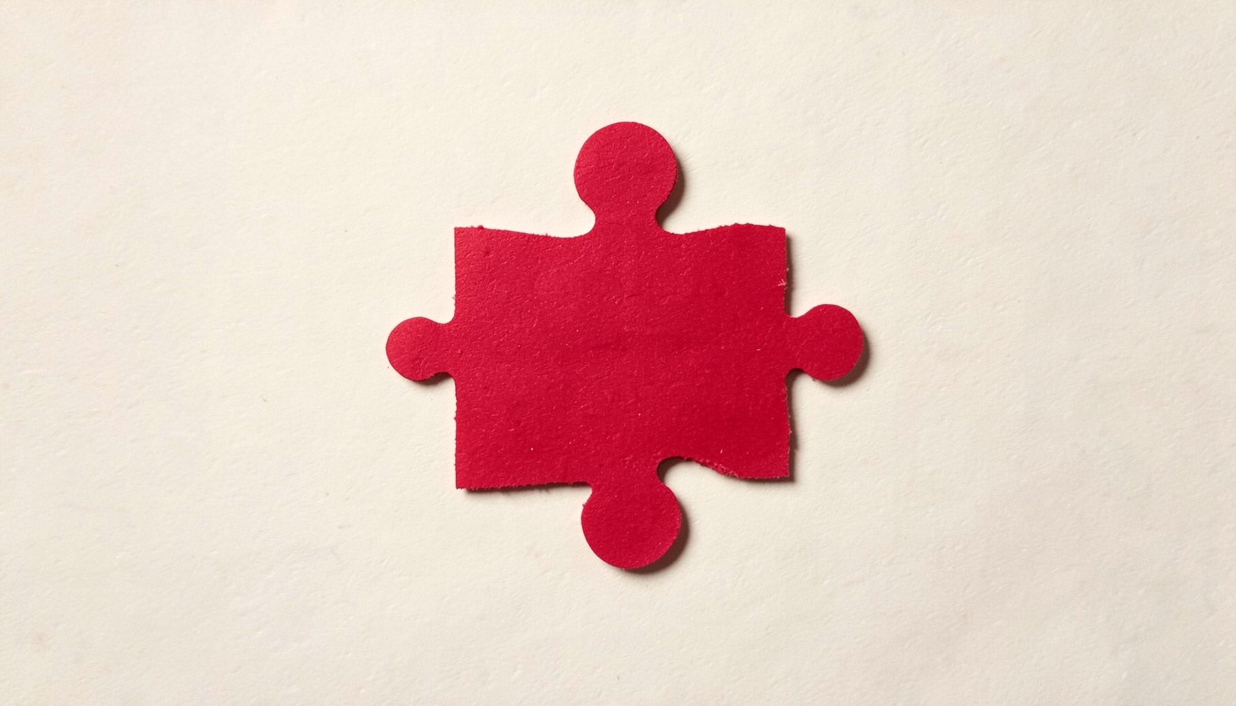 A small layered paper cut-out collage of a jigsaw piece in crimson red on cream paper, calm mood