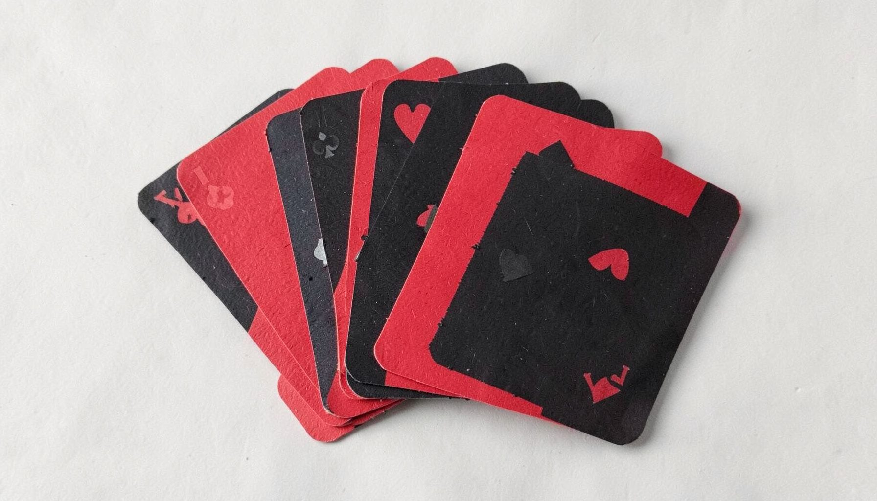 A small layered paper cut-out collage of playing cards fanned out in red and black, classic mood