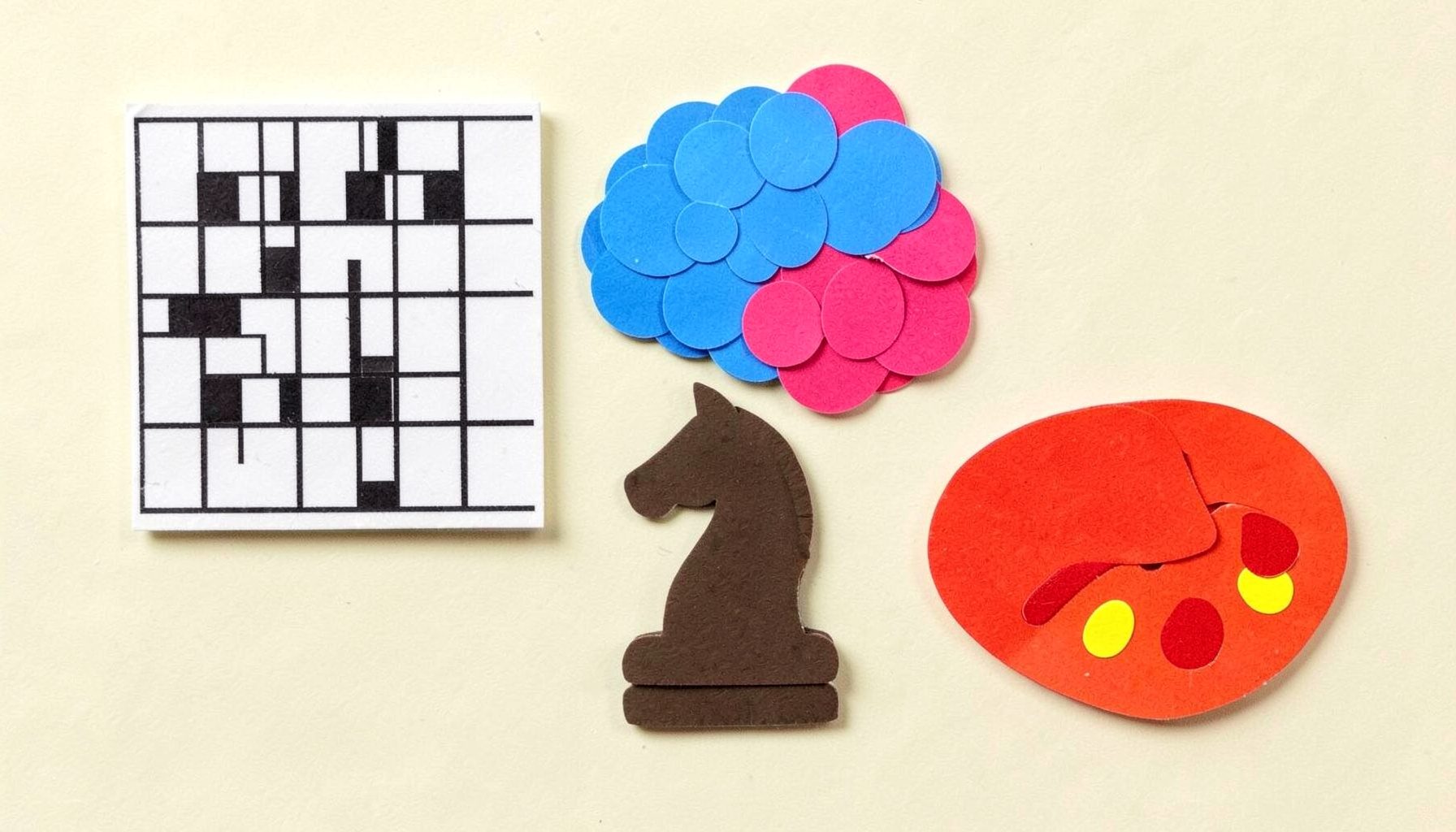 Layered paper cut-out collage of colorful game icons: a crossword grid in black and white, a bubble cluster in bright blue, and a pencil