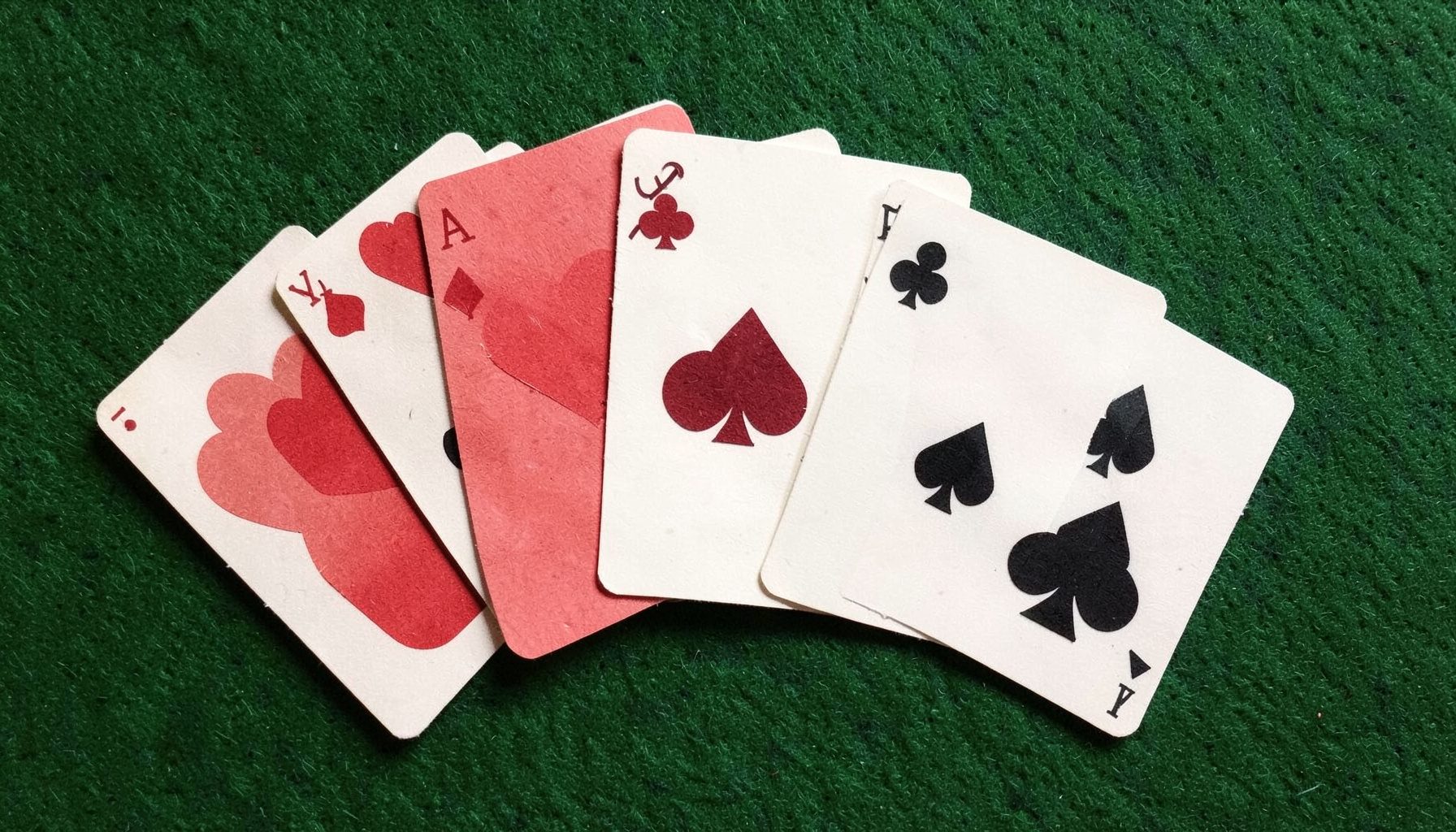 A layered paper cut-out collage of playing cards fanned across a deep green felt surface, with hearts, spades, diamonds, and clubs in red and black.